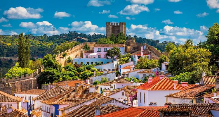 Charmante mittelalterliche Stadt Óbidos mit weiß getünchten Häusern, Terrakottadächern und Burgmauern unter einem lebendigen blauen Himmel.