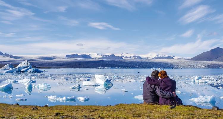 Ein Paar umarmt sich, während es die schwimmenden Eisberge in der spiegelglatten Gletscherlagune Jokulsarlon bewundert.