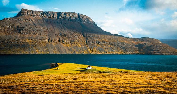 Einsam gelegener Bauernhof auf einer grasbewachsenen Halbinsel, umrahmt von tiefem Fjord und aufragenden Basaltklippen in den Westfjorden.