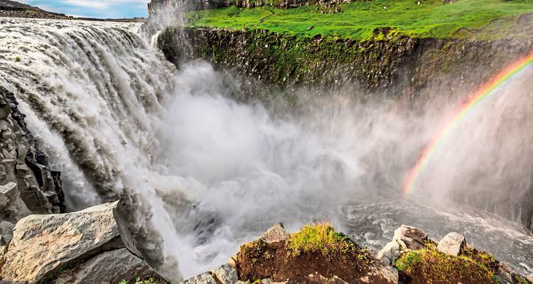 Der gewaltige Wasserfall Dettifoss stürzt in einen nebeligen Canyon und wird durch einen leuchtenden Regenbogen akzentuiert.