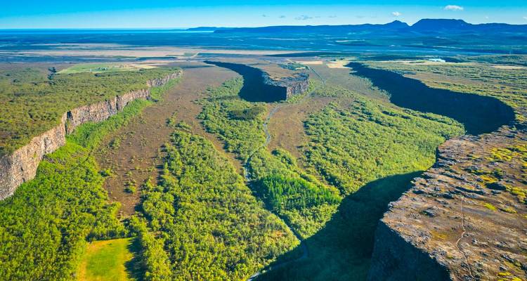 Luftaufnahme der Hufeisenklippen des Asbyrgi-Canyons und des bewaldeten Tals, das sich zu entfernten Vulkanrücken erstreckt.