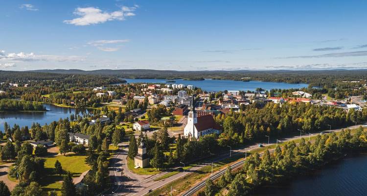 Luftaufnahme eines Panoramas einer finnischen Seeuferstadt, umgeben von Wäldern und Wasserwegen an einem sonnigen Tag.