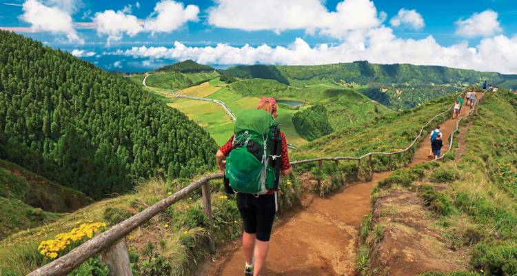 Rucksacktouristen wandern auf einem malerischen Bergkammweg mit Blick auf Flickenteppich-Felder und Kratterseen auf São Miguel.