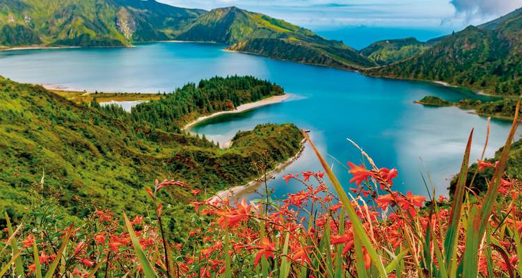 Die strahlend blaue Lagoa do Fogo, umrahmt von üppig grünen Hängen und roten Wildblumen.