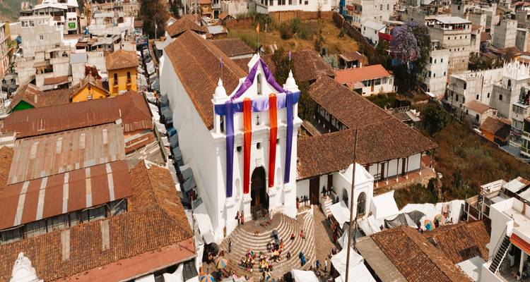 Toma panorámica con dron de la iglesia blanca de Chichicastenango adornada con banderines coloridos entre los densos techos del pueblo.