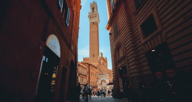 Enge mittelalterliche Gasse, die sich auf Sienas Piazza del Campo öffnet, mit dem aufragenden Torre del Mangia.