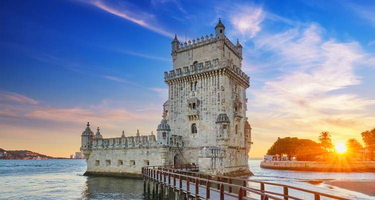 Der Turm von Belém steht bei Sonnenuntergang neben dem Fluss Tejo mit warmem Licht auf seiner Steinfassade.