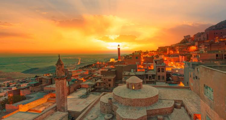 De gouden zonsondergang baadt het heuvelachtige stadsgezicht van Mardin in warm licht met gloeiendo minaretten en daken.