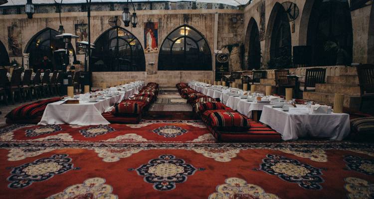 Lange lage tafels met kussens en sierlijke tapijten klaargemaakt voor het diner in een traditioneel binnenplaatsrestaurant.