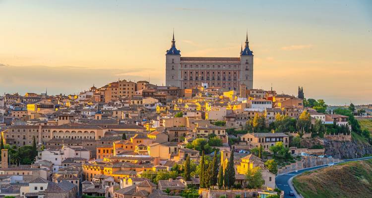 Le coucher de soleil doré illumine le paysage urbain médiéval de Tolède avec l'Alcázar dominant au-dessus.