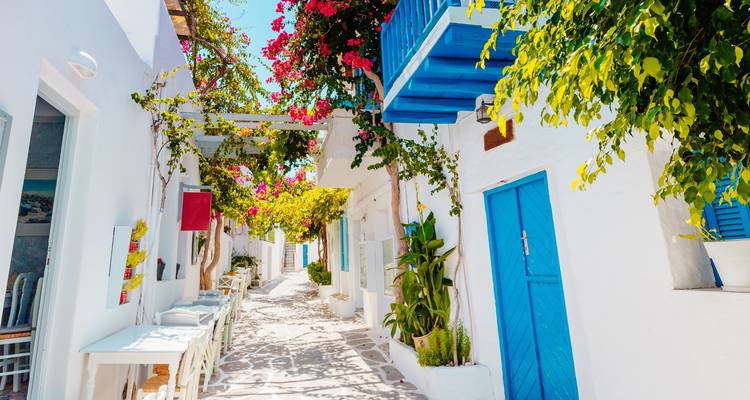 Charmante enge Gasse mit weißen Gebäuden, blauen Türen und leuchtenden Blumen in den Kykladen.