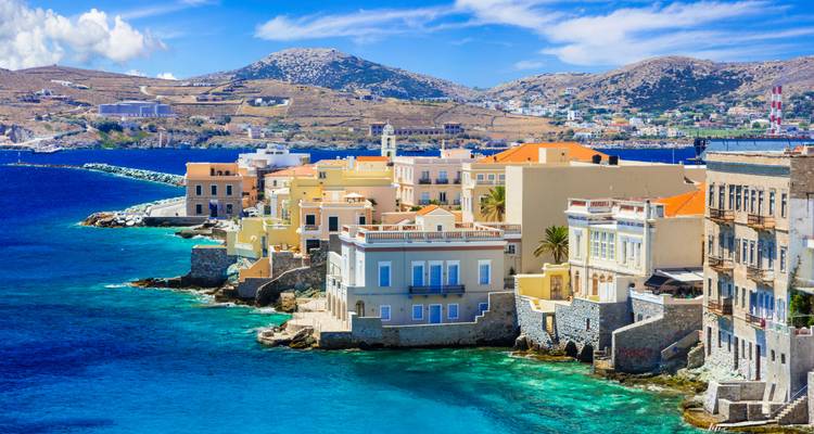 Farbenfrohe Hafenhäuser von Syros, die an der felsigen Küstenlinie neben dem türkisfarbenen Ägäischen Meer thronend.