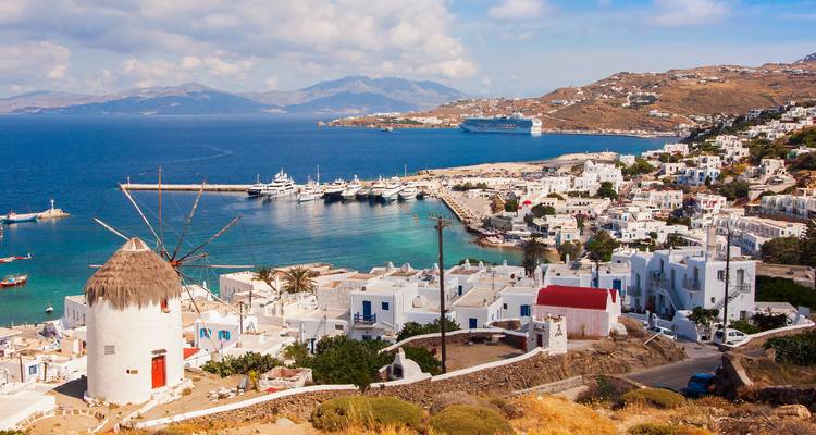 Panoramisch uitzicht over de haven van Mykonos met witte huisjes, een molen en de diepblauwe Egeïsche Zee.