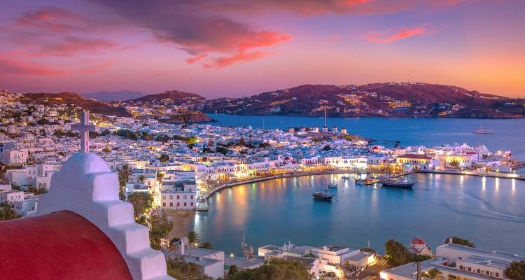 Schemering panorama van de witgekalkte huizen van Mykonos-stad en de haven die oplichten onder roze lucht.