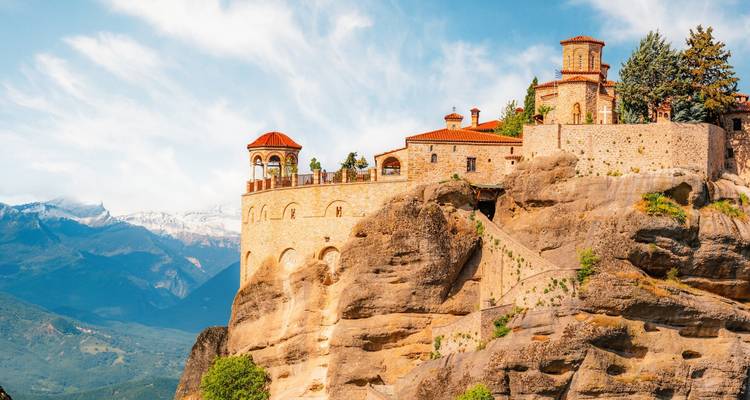 Historisch Meteora-klooster op dramatische rotspilaren met sneeuwbedekte bergen daarachter.