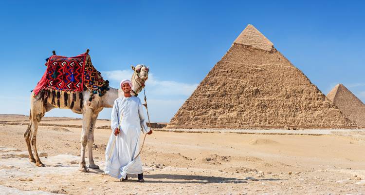 Ein traditionell gekleideter Kamelführer posiert neben seinem Kamel, während die Große Pyramide hinter ihnen aufragt.