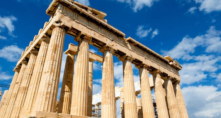 Opwaarts perspectief van oude Parthenon-zuilen omlijst door een levendige blauwe lucht met witte wolken.