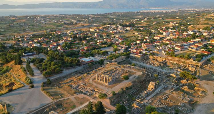 Drone-opname onthult de ruïnes van het antieke Corinth en de omliggende moderne stad met zee en bergen in de verte.