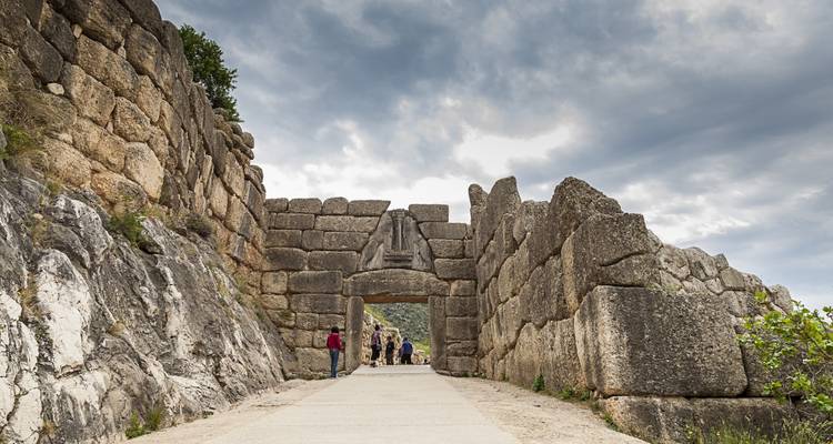 Bezoekers lopen door de indrukwekkende stenen Leeuwenpoort van het oude citadel in Mycene onder dramatische wolken.