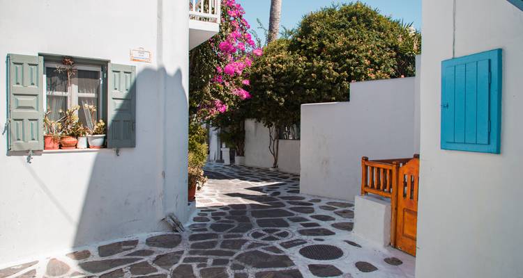 Rustige smalle steeg in Mykonos met blauwe luiken en felle bougainville.