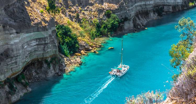 Un catamaran lumineux naviguant à travers un canyon d'un turquoise éclatant, flanqué de falaises rocheuses abruptes et de buissons verdoyants.