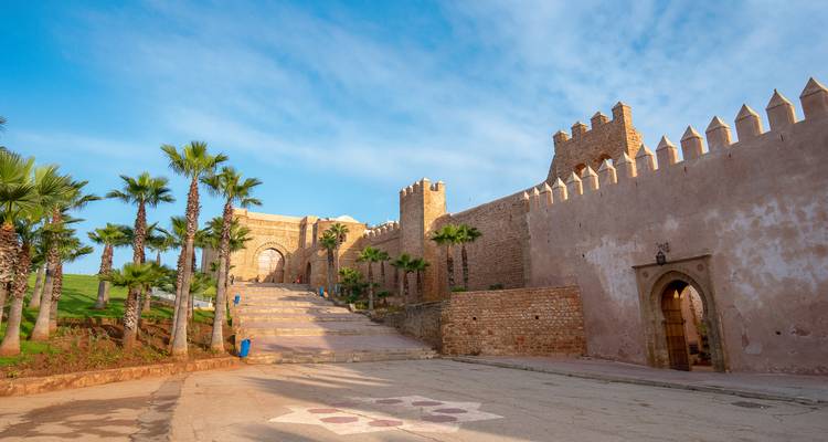Historisches befestigtes Tor und Steinmauern mit einer von Palmen gesäumten Treppe, die im Morgenlicht in Rabat liegt.