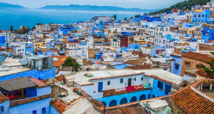 Panoramablick über die blau angestrichenen Häuser von Chefchaouen, eingebettet in den Nebel der Rifberge.