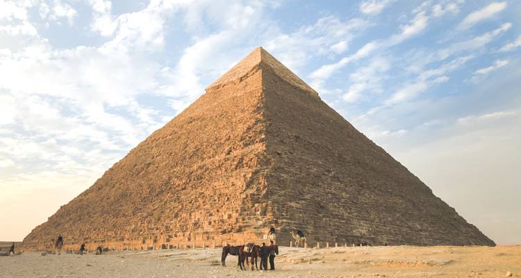 La majestueuse Grande Pyramide domine le paysage désertique avec des chevaux et des cavaliers à sa base