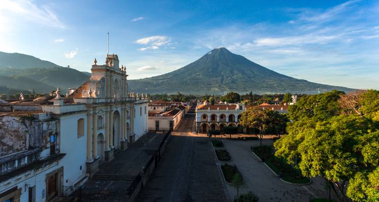 Vista aérea matutina sobre Antigua con la catedral en primer plano y un imponente volcán más allá.