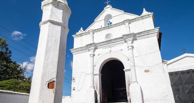 Iglesia colonial blanca y un pilar adyacente se destacan claramente contra un cielo azul despejado.