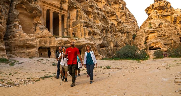 Viajeros caminando a través de un impresionante cañón de arenisca hacia fachadas antiguas talladas