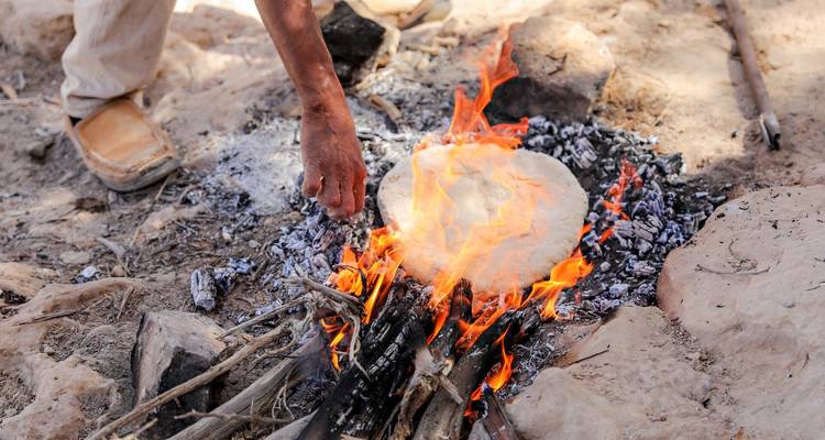 Primer plano de pan plano siendo horneado directamente sobre un fuego de leña abierto en el desierto
