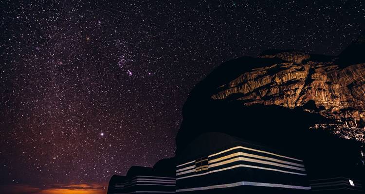 Cielo nocturno lleno de estrellas brillantes sobre tiendas beduinas a rayas y una cara de roca escarpada