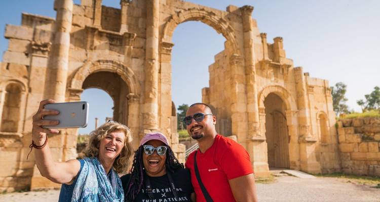 Des amis qui se prennent en selfie devant l'Arc d'Hadrien parmi les ruines antiques de Jérash.