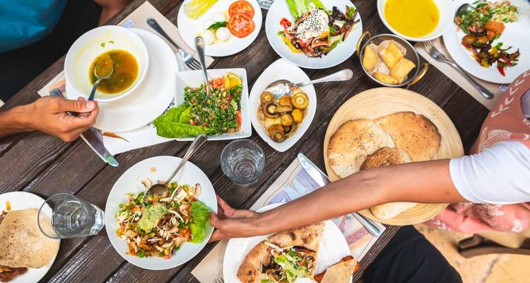 Assortiment coloré de mezze jordaniens sur une table en bois avec des convives qui se servent des plats.