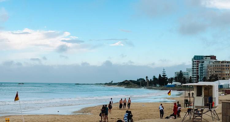 Les baigneurs pratiquant des sports et nageant le long d'une plage urbaine sous un ciel bleu dégagé