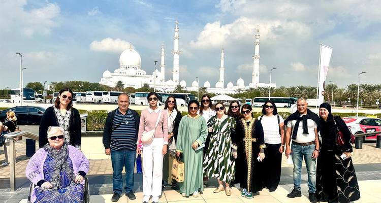 Le groupe de touristes pose devant les dômes blancs étincelants et les minarets de la Grande Mosquée Sheikh Zayed sous des nuages épars.