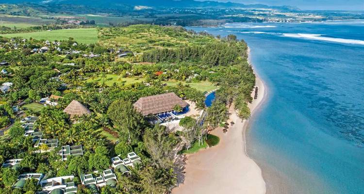 Aerial view of beachfront resort complex bordered by lush vegetation and a long sandy shore.