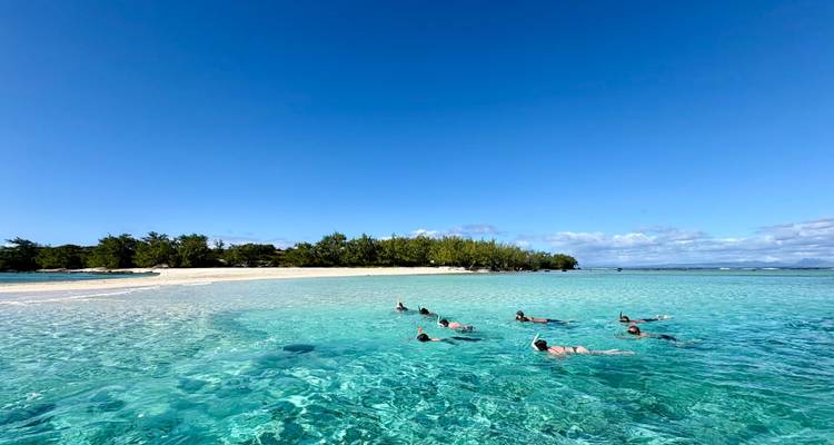 Visitors floating and snorkeling in shallow crystal-clear lagoon off a white sandy island beach.