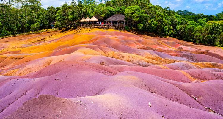 Vibrant multicolored dunes of Chamarel Seven Coloured Earths with forest and thatched lookout hut.