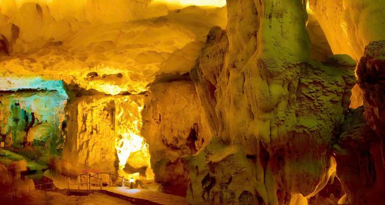 Illuminated cave chamber with dramatic yellow and green stalactites and stalagmites.