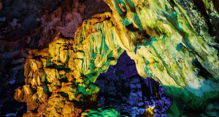 Colorfully lit rock formations arch inside a large limestone cave.