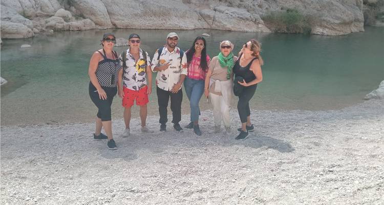 Six voyageurs se tiennent debout sur du gravier à côté d'une piscine turquoise entourée de murs rocheux blancs.
