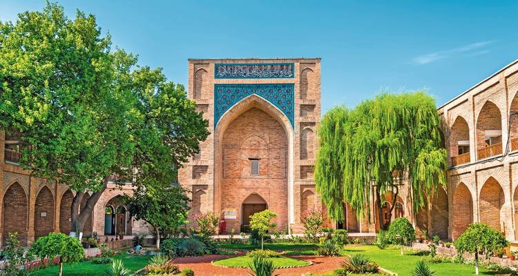 Prächtige Backsteinmadrasa mit gewölbtem, blauem Flieseneingang, umgeben von üppigen Gärten im Innenhof von Taschkent.