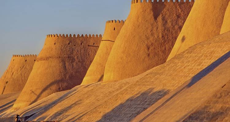 Die massiven Lehmziegelmauern der antiken Festung Itchan Kala leuchten in goldenem Abendlicht in Chiva.