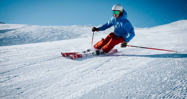 Un skieur en tenue colorée trace des virages dans la neige fraîchement damée sur un versant montagneux ensoleillé.