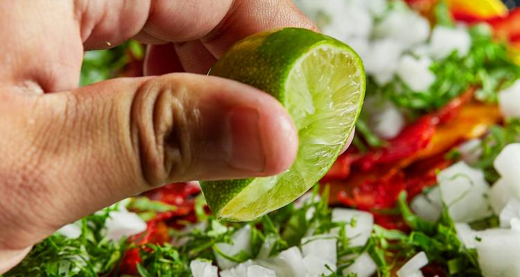 Gros plan d'une main pressant un quartier de citron vert frais sur des oignons rouges finement dés et des herbes aromatiques.