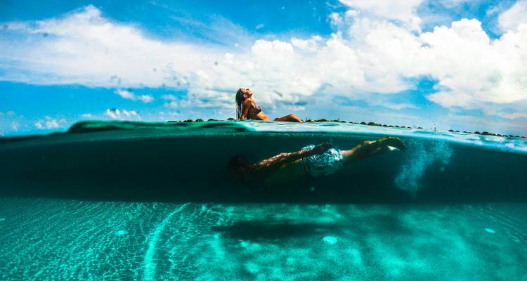 Photo en deux niveaux créative montrant une femme allongée au soleil au bord d'une piscine au-dessus de l'eau tandis qu'un homme nage sous l'eau sous un ciel ensoleillé.