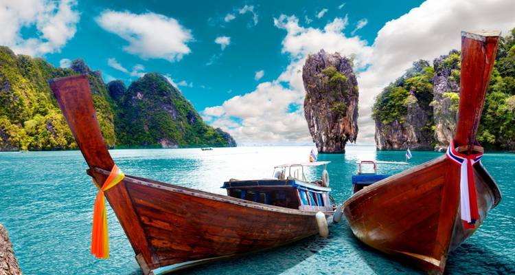 Deux bateaux traditionnels à longue queue ancrés dans des eaux turquoise face aux imposants pics calcaires du Phang Nga Bay.