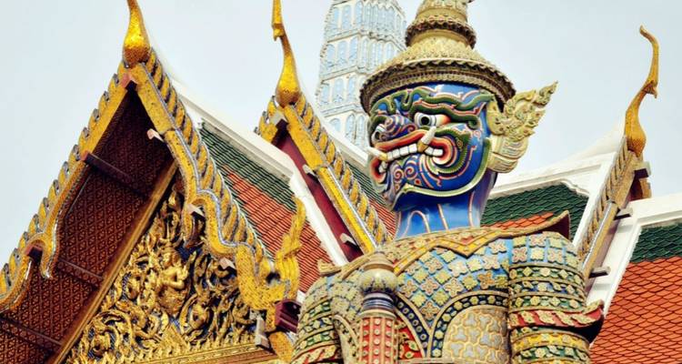 Gros plan d'une statue de démon gardien aux couleurs vives au Grand Palais de Bangkok avec des tuiles de toit complexes.